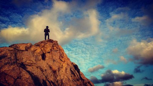 Low angle view of male hiker standing on rocky mountain against blue sky