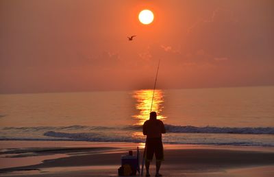 Rear view of silhouette man on beach against sky during sunset