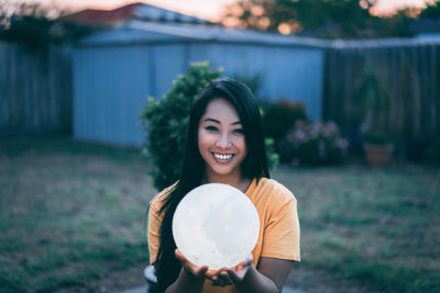 Portrait of smiling young woman holding illuminated ball on field during sunset