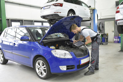 Car mechanic in a workshop using diagnostics computer at car