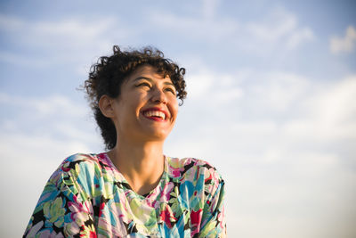 Low angle view of cheerful woman against cloudy sky