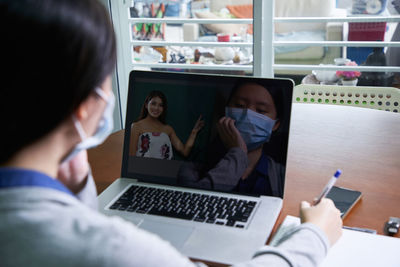 Rear view of girl wearing mask using laptop at home