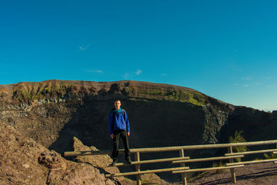 Portrait of young man standing on railing against blue sky