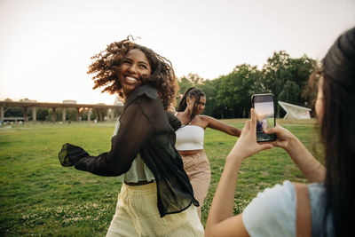 Teenage girl photographing happy female friends dancing in park