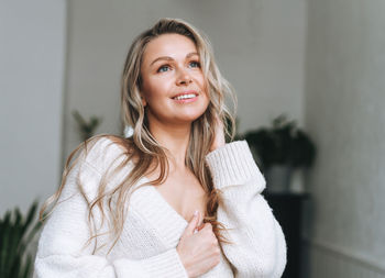 Blonde smiling woman 35 year plus clean fresh face and hands with long hair in cozy knitted cardigan 