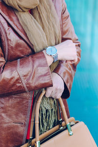 Midsection of woman with bag standing against blue wall