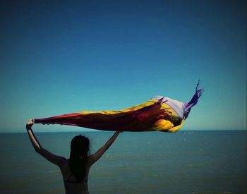 Rear view of woman walking in sea against clear blue sky