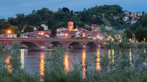 Illuminated bridge over lake against buildings at dusk