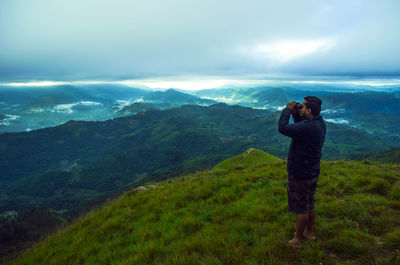 Man looking through binoculars while standing on mountain against sky