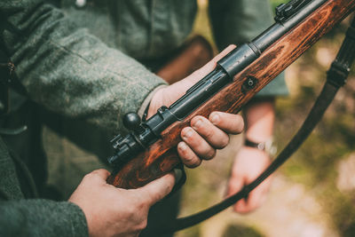 Midsection of army soldier holding gun while standing outdoors