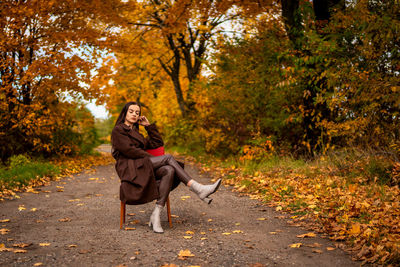 Portrait of a young woman with old armchair in a brown coat in autumn