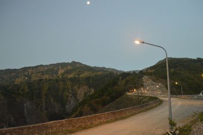 Road by illuminated street light against clear sky at night