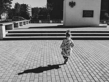 Rear view of girl walking on footpath in city during sunny day