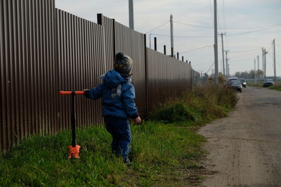 Rear view of boy standing with metal fence against sky