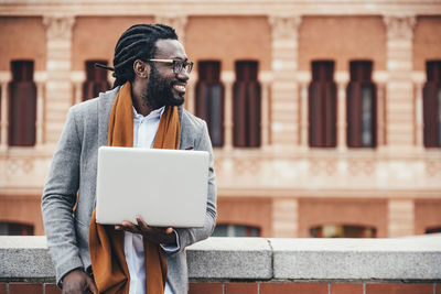 Businessman using laptop while standing against building