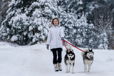 Full length of woman walking with dogs on field against trees during winter