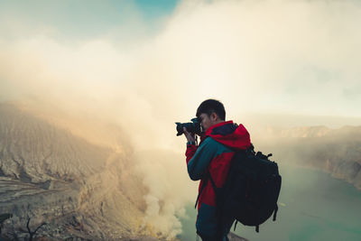 Side view of man photographing with digital camera on mountain