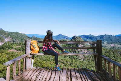 Woman sitting on bench against mountains against clear sky