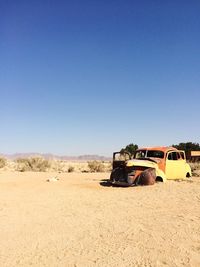 Abandoned vintage car in desert against clear blue sky