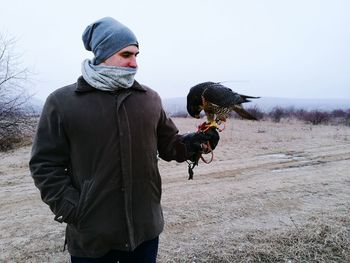 Man holding falcon on field against sky