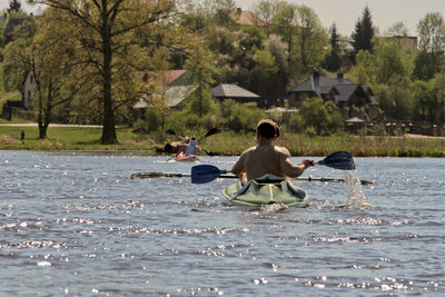 Rear view of men canoeing in river against sky