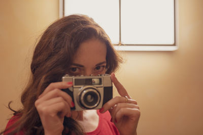 Portrait of woman photographing against yellow wall