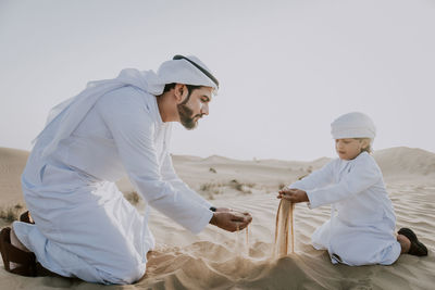 Father and son enjoying while crouching in desert