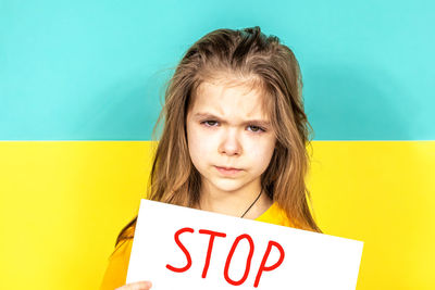 A crying girl holds a stop poster in her hands against the background of the ukrainian flag.