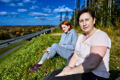 Happy friends sitting on plants against sky