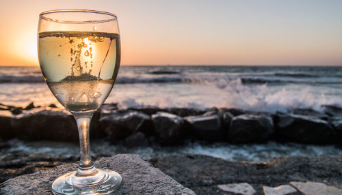 Close-up of wineglass against sky at sunset