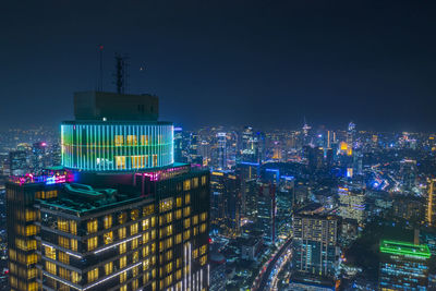 Illuminated modern buildings in city against sky at night