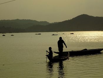 Silhouette people on boat in lake against sky during sunset