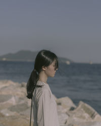 Side view of thoughtful woman standing at beach against sky