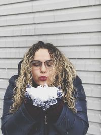 Young woman blowing snow while standing against wall