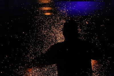 Silhouette man standing against illuminated sky at night