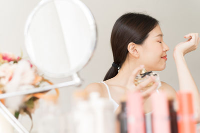 Young woman smelling perfume at home