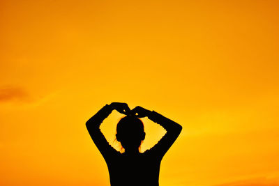 Silhouette woman standing against orange sky