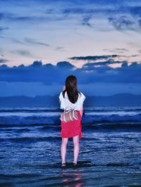 Rear view of woman standing at beach against sky