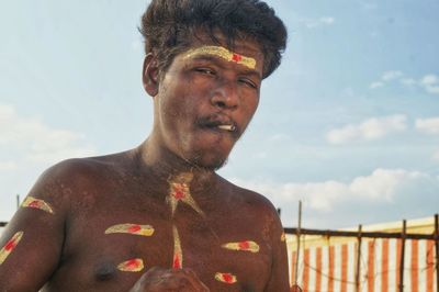 Low angle portrait of shirtless mid adult man smoking cigarette against sky