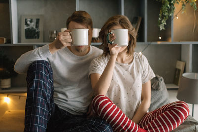 Couple holding mugs while sitting on sofa at home