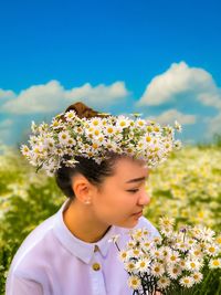 Young woman with yellow flowers on field against sky