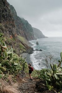 Man standing on rock by sea against sky