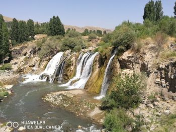 Scenic view of waterfall in forest against sky