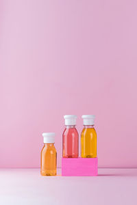 Close-up of multi colored bottles on shelf against pink background