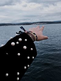 Close-up of hand by sea against sky