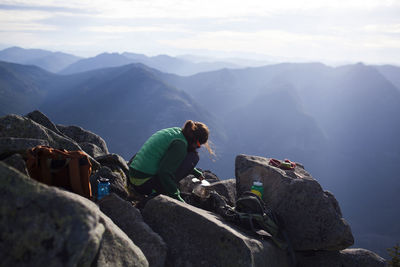 Hiker boiling water while crouching on rocks against mountains