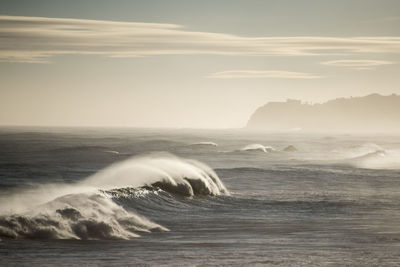 Sea waves splashing on shore against sky