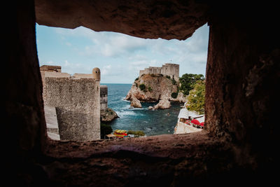 Buildings by sea against sky seen through window