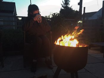 Woman sitting by tree against sky at night