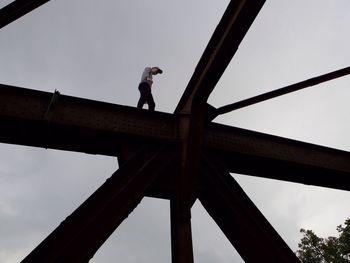 Low angle view of man standing on metallic structure at construction site against sky